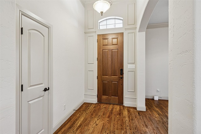 foyer with baseboards, arched walkways, a textured wall, ornamental molding, and dark wood-style flooring