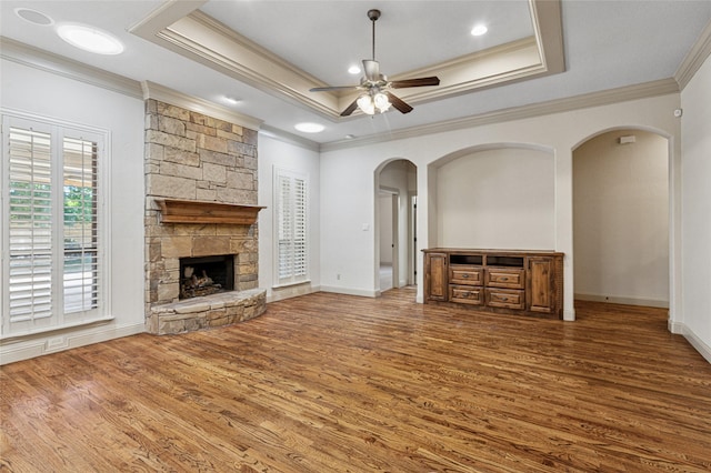 unfurnished living room featuring arched walkways, a fireplace, a raised ceiling, a ceiling fan, and wood finished floors