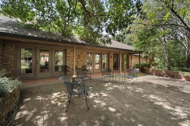 rear view of house with a shingled roof, a patio area, french doors, and brick siding