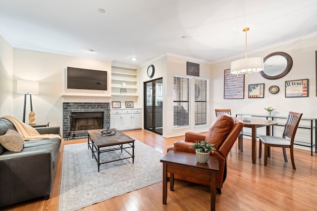 living area with ornamental molding, a brick fireplace, built in features, and light wood finished floors