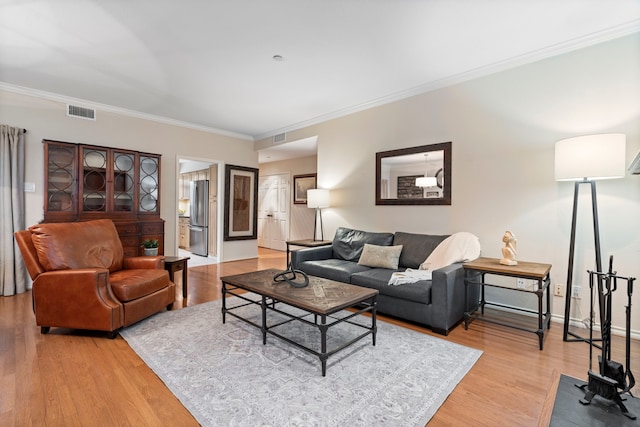 living room with ornamental molding, wood finished floors, visible vents, and baseboards