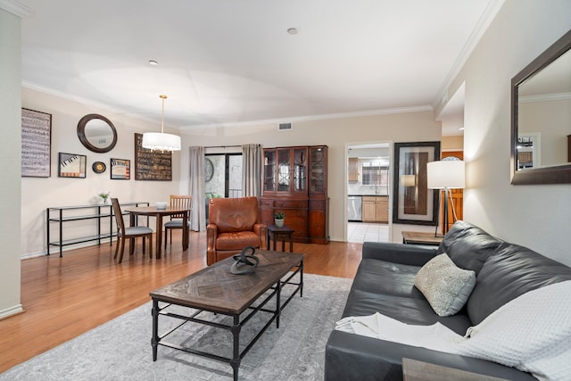 living room with light wood-type flooring, baseboards, visible vents, and ornamental molding