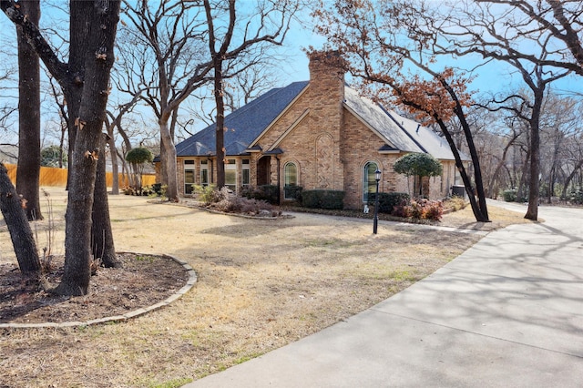 view of side of property with a shingled roof, a chimney, fence, a yard, and brick siding