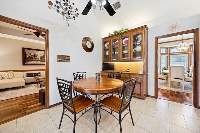 dining space featuring light tile patterned floors, ceiling fan with notable chandelier, visible vents, baseboards, and vaulted ceiling