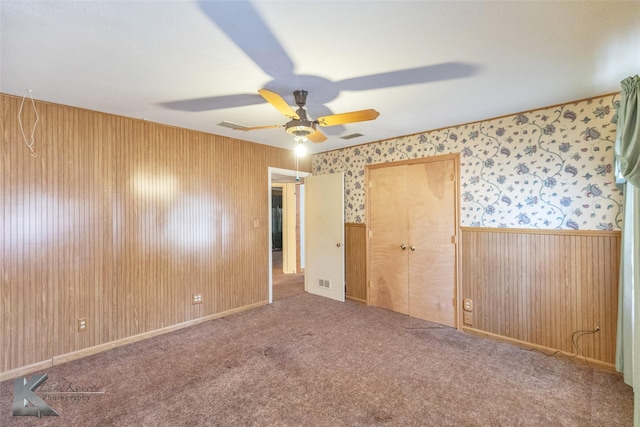 unfurnished bedroom featuring carpet floors, a wainscoted wall, visible vents, a ceiling fan, and wallpapered walls