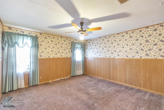 unfurnished room featuring carpet, a wainscoted wall, a ceiling fan, wood walls, and wallpapered walls