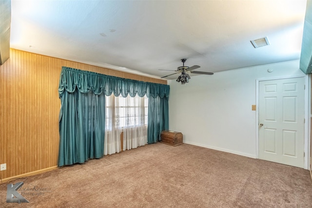 spare room with wood walls, carpet, visible vents, and a ceiling fan