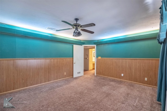 empty room featuring a wainscoted wall, visible vents, a ceiling fan, carpet flooring, and wood walls