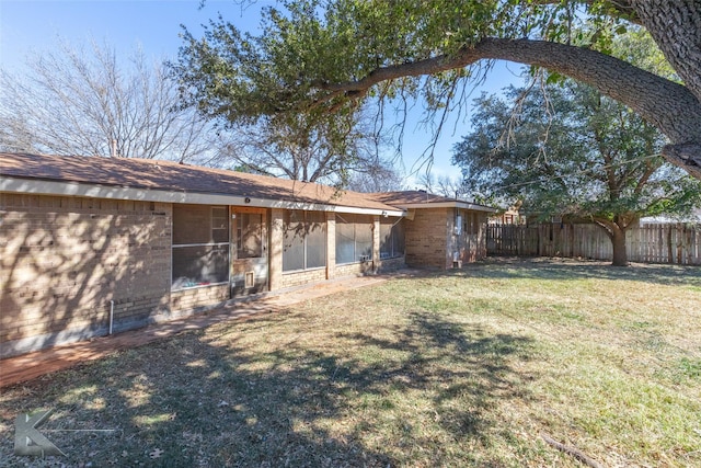 back of house with a sunroom, brick siding, fence, and a lawn