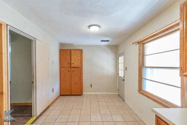 empty room with light tile patterned floors, baseboards, visible vents, and a textured ceiling