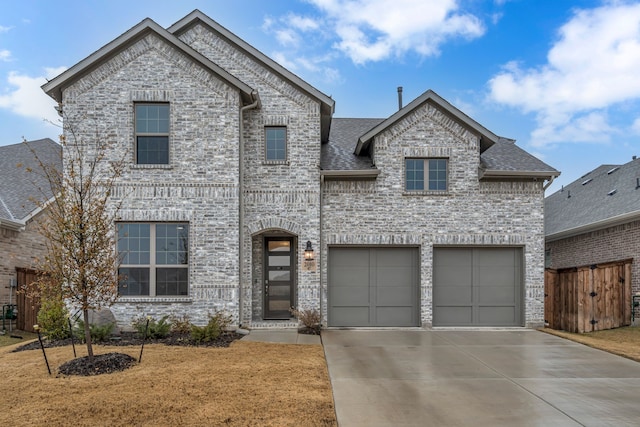 french country style house with a shingled roof, brick siding, driveway, and a garage