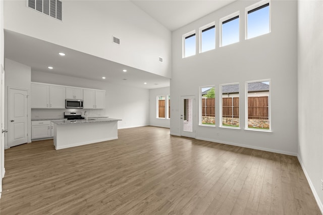 2720 Green River Rd, Royse City, TX 75189 - unfurnished living room with a towering ceiling, light wood-style floors, a sink, baseboards, and recessed lighting