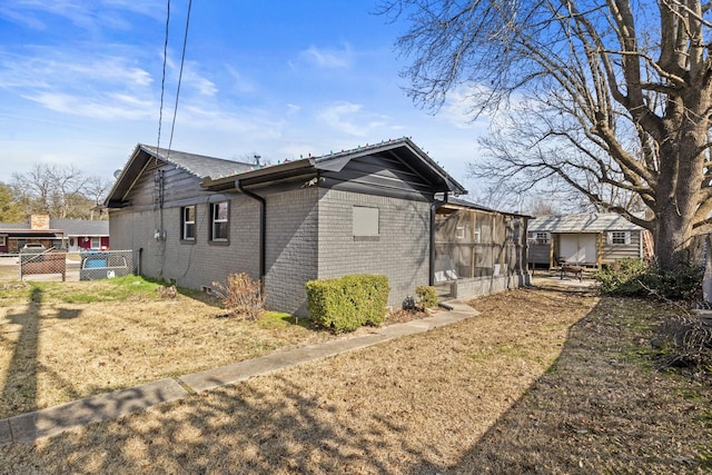 view of side of home with a yard, a sunroom, brick siding, and fence