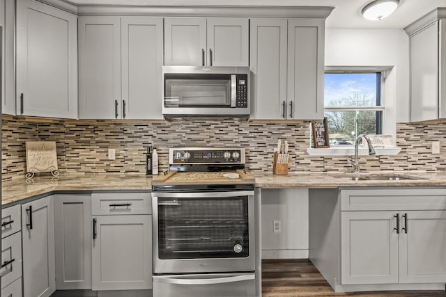 kitchen with appliances with stainless steel finishes, backsplash, dark wood-type flooring, light stone counters, and a sink