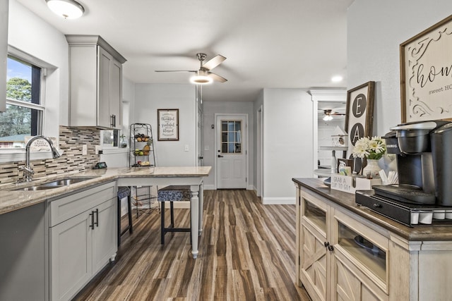 kitchen featuring a sink, a ceiling fan, baseboards, backsplash, and dark wood finished floors