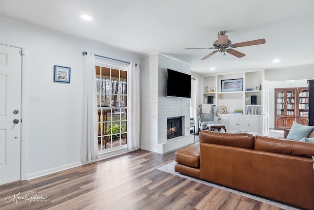 living room with wood finished floors, a ceiling fan, baseboards, ornamental molding, and a brick fireplace