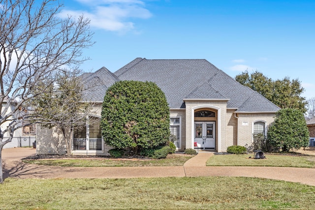 french provincial home featuring a front yard, brick siding, and roof with shingles