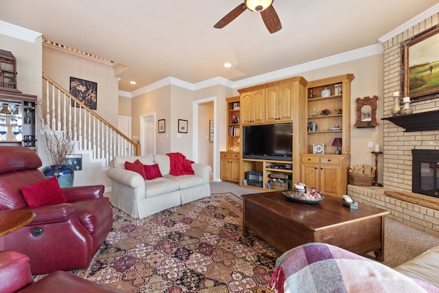 living area with ceiling fan, stairway, a brick fireplace, carpet, and crown molding