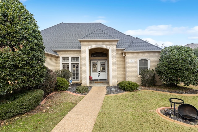 french country style house with roof with shingles, a front lawn, and brick siding