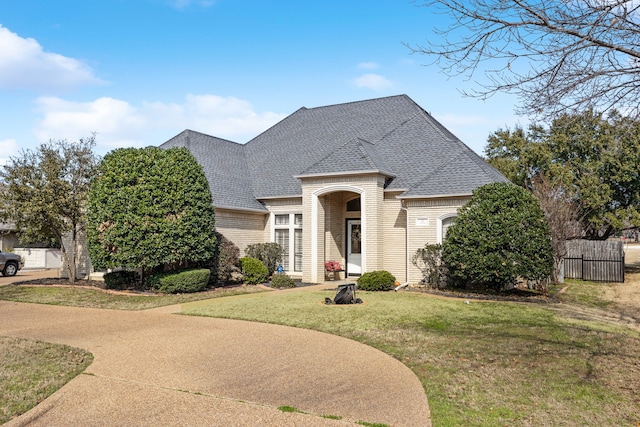 view of front facade with a shingled roof, a front yard, fence, and brick siding