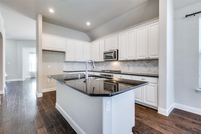 kitchen featuring a kitchen island with sink, stainless steel microwave, dark wood finished floors, and white cabinetry