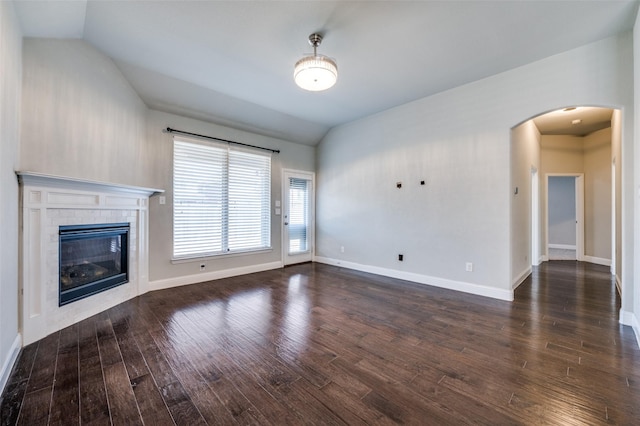 unfurnished living room with arched walkways, dark wood finished floors, a glass covered fireplace, vaulted ceiling, and baseboards