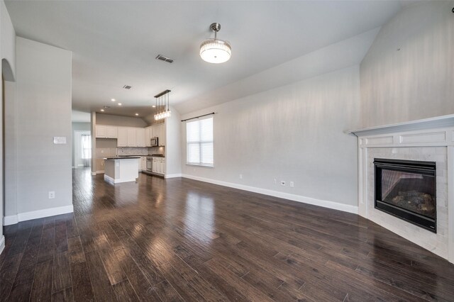 unfurnished living room featuring dark wood-style flooring, visible vents, baseboards, and a tiled fireplace