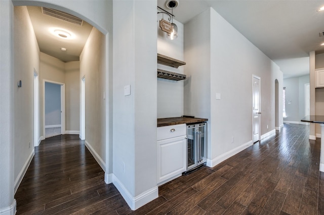 hall with visible vents, arched walkways, beverage cooler, and dark wood-type flooring