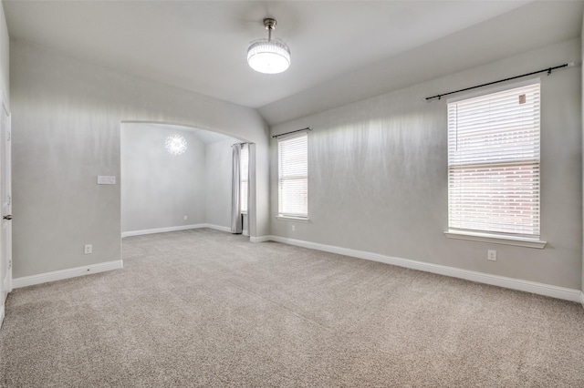 carpeted spare room with lofted ceiling, baseboards, and arched walkways