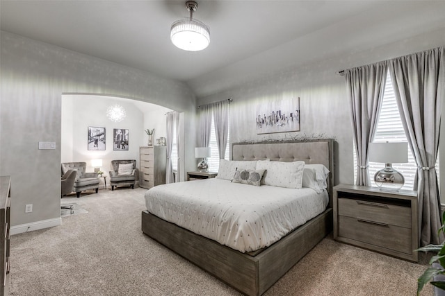 bedroom with arched walkways, light carpet, baseboards, and multiple windows