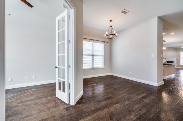 unfurnished dining area with dark wood-style flooring, visible vents, a sink, baseboards, and ceiling fan with notable chandelier