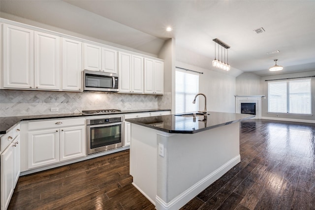 kitchen featuring stainless steel appliances, dark countertops, a sink, and an island with sink