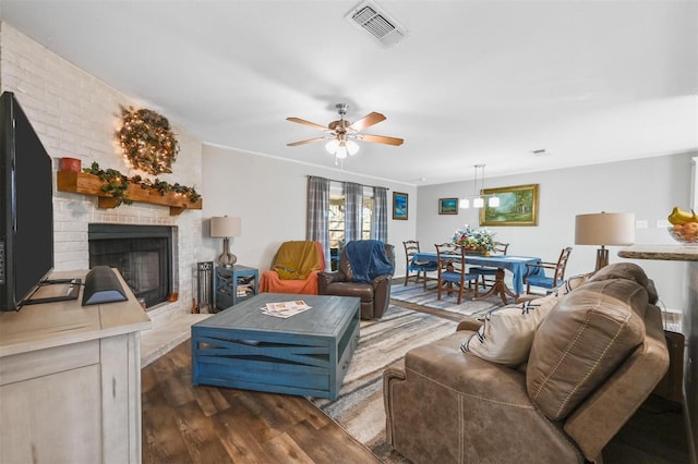 living area with dark wood-style flooring, a brick fireplace, visible vents, and a ceiling fan