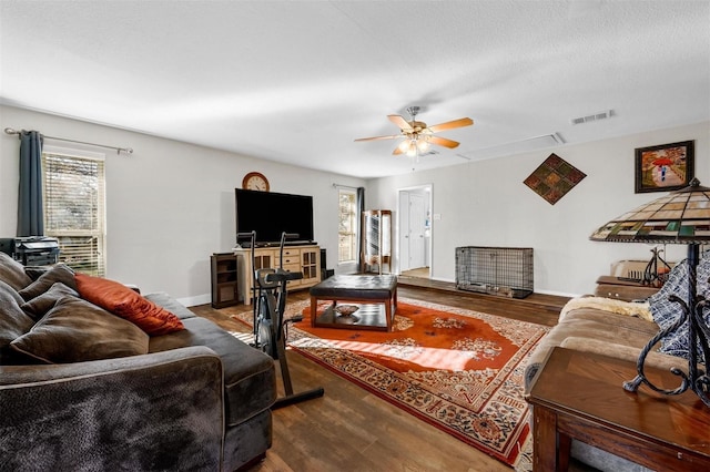 living area with a ceiling fan, wood finished floors, visible vents, and baseboards