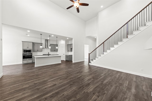 551 Baker Ct, Fate, TX 75189 - unfurnished living room featuring a ceiling fan, stairway, dark wood-style flooring, baseboards, and a high ceiling