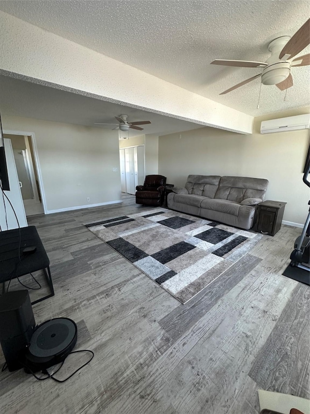 living area featuring a wall unit AC, ceiling fan, a textured ceiling, wood finished floors, and baseboards