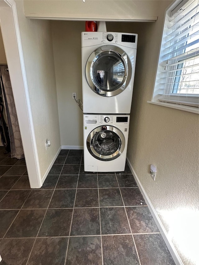 laundry room with laundry area, dark tile patterned floors, stacked washing maching and dryer, and baseboards