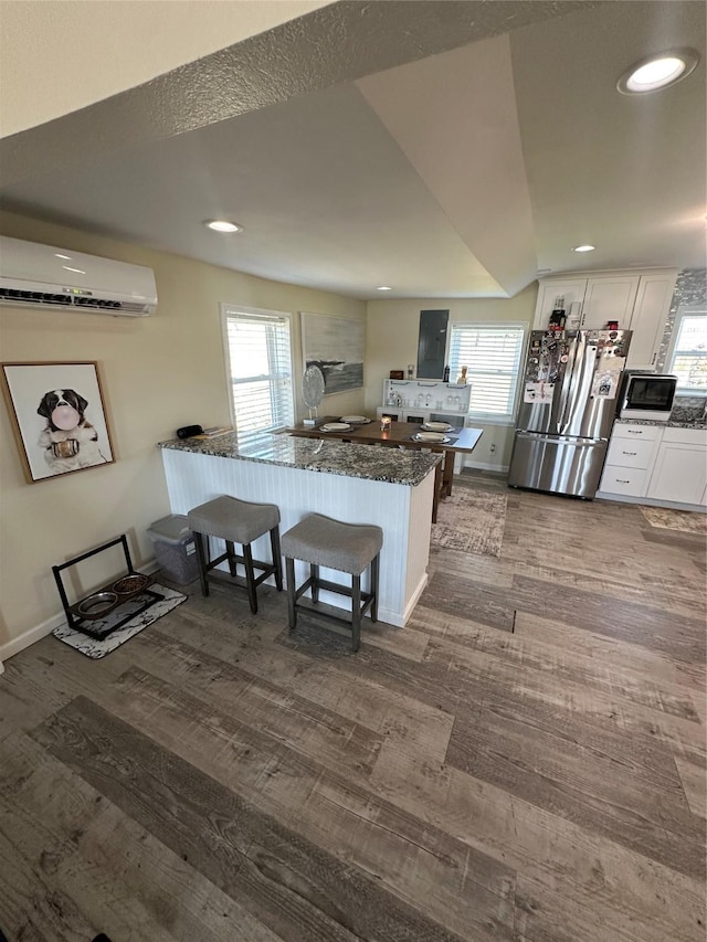 kitchen with a breakfast bar area, a peninsula, white cabinets, freestanding refrigerator, and a wall mounted air conditioner