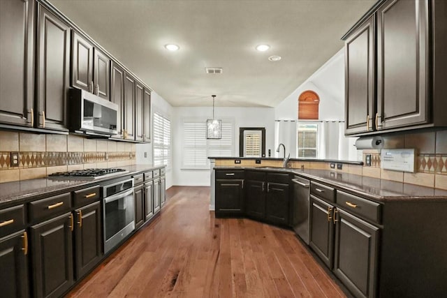 kitchen with a wealth of natural light, tasteful backsplash, appliances with stainless steel finishes, and dark wood-style flooring