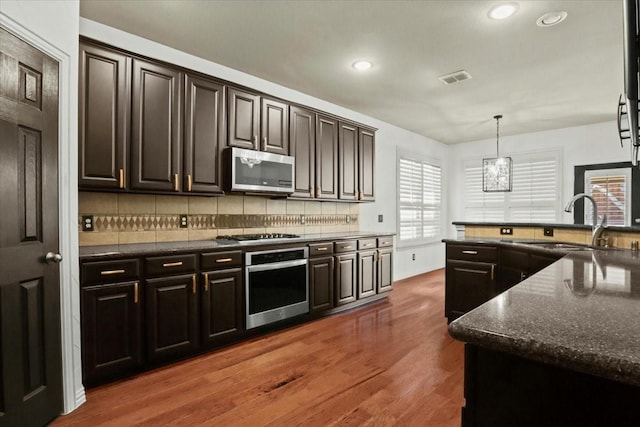 kitchen featuring dark wood-style flooring, pendant lighting, stainless steel appliances, tasteful backsplash, and a sink