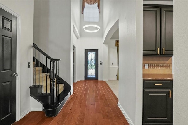 entryway with stairs, wood finished floors, a towering ceiling, and baseboards