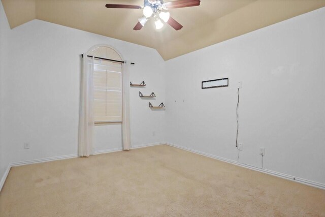 spare room featuring light carpet, ceiling fan, vaulted ceiling, and baseboards