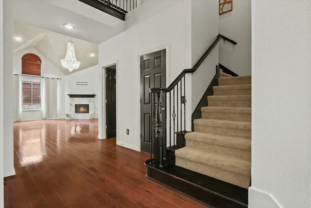 stairs featuring high vaulted ceiling, a fireplace, hardwood / wood-style flooring, and baseboards