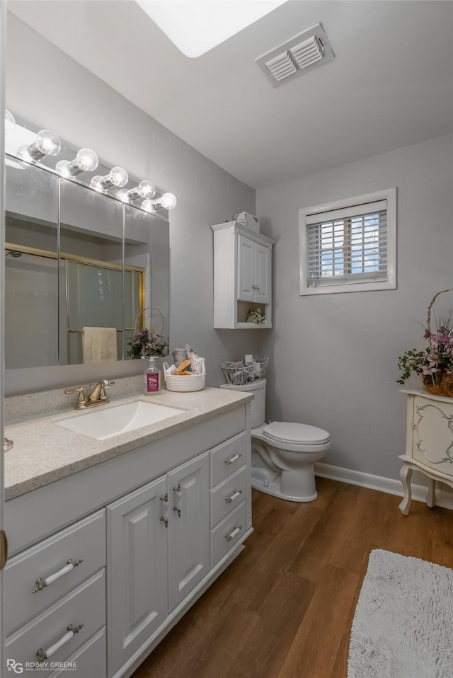 bathroom featuring toilet, wood finished floors, vanity, visible vents, and baseboards