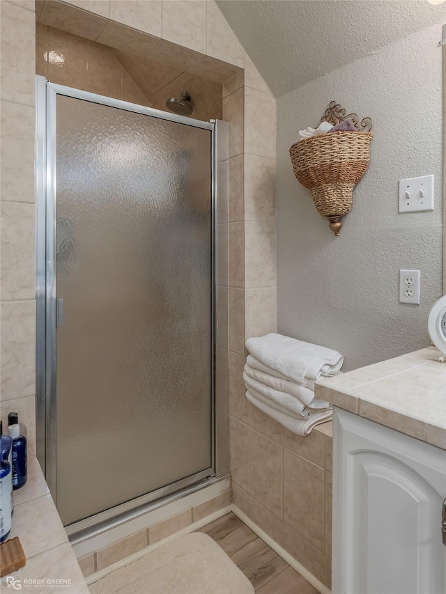 bathroom with lofted ceiling, a textured wall, wood finished floors, vanity, and a shower stall