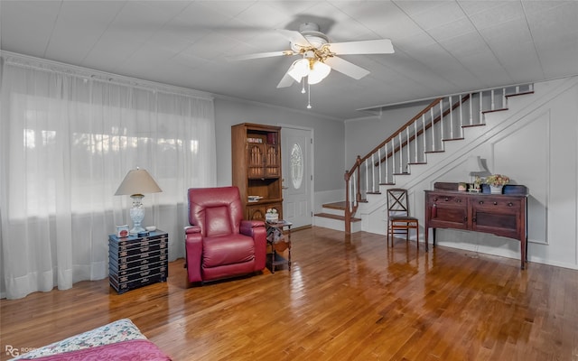 living area with ornamental molding, a ceiling fan, stairway, and wood finished floors