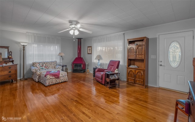 living area with a wood stove, plenty of natural light, crown molding, and wood finished floors