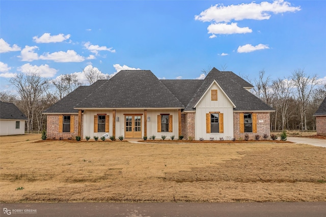 modern farmhouse with french doors, board and batten siding, a front lawn, and brick siding