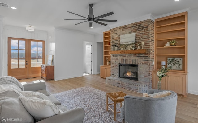 living room featuring light wood-style floors, a fireplace, visible vents, and crown molding