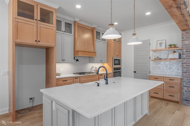 kitchen featuring wood finish floors, glass insert cabinets, appliances with stainless steel finishes, a kitchen island with sink, and a sink